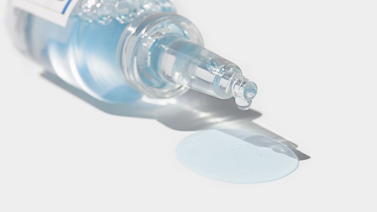 Veranum Cicaultra Moisture Ampoule lying on white with hydrating serum dripping from its glass tip into a small pool