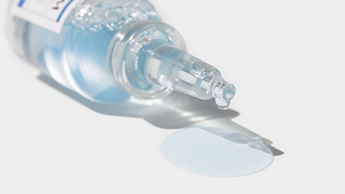 Clear hydrating liquid dripping from a glass ampoule tip — the humectant formula behind a good Korean face mist